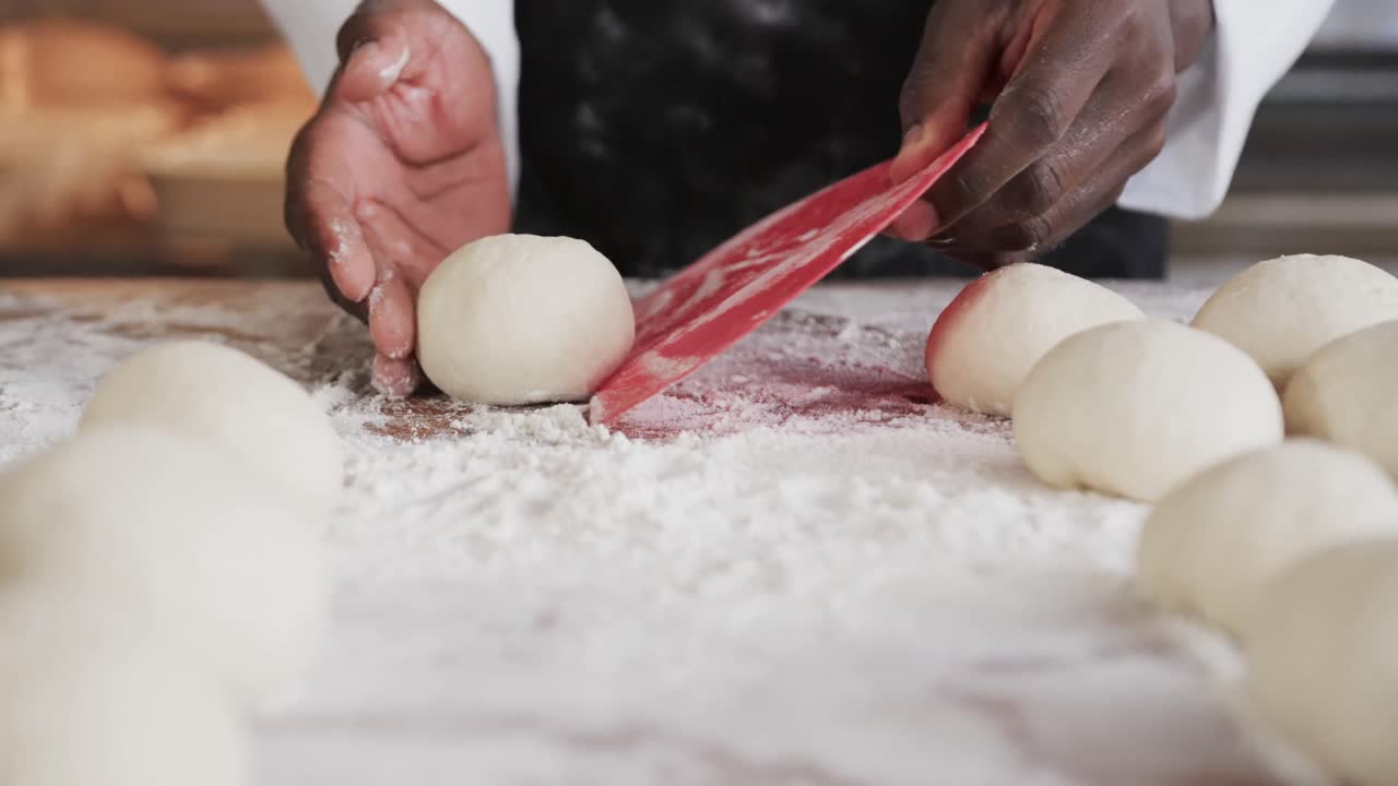 Afroamerikkalainen miesleipuri työskentelemässä leipomon keittiössä, valmistamassa leipäsämpylöitä taikinasta hidastettuna.