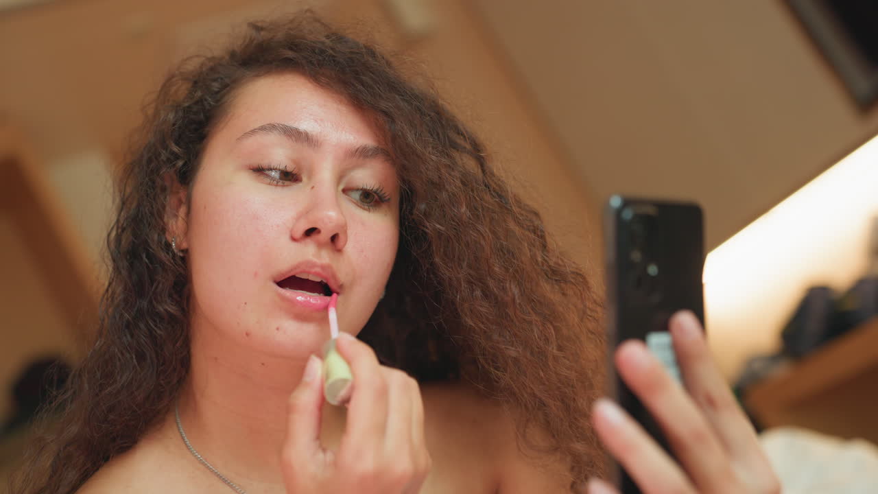 Confident Latina hotel worker fixing lipstick before first meeting. Poised professional woman from Latin America adjusting lipstick while looking at her reflection in bedside mirror
