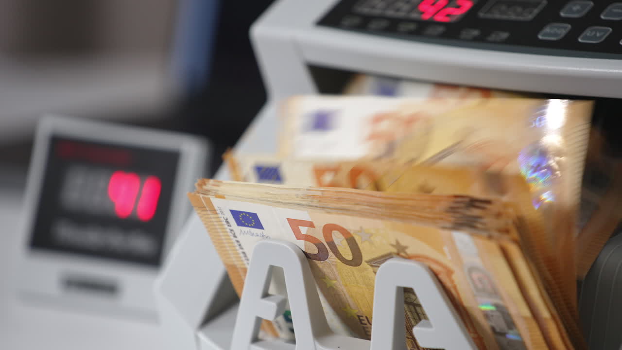 Orange banknotes of fifty euro turning quickly in cash counting machine. Numbers changing at the counter in blur. Close up.