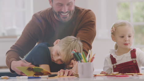 Father-With-Children-At-Home-Doing-Craft-And-Making-Picture-From-Leaves-In-Kitchen