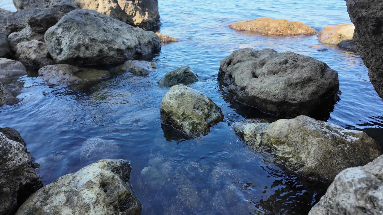 Acque calme lambiscono la costa rocciosa mentre il sole proietta un bagliore dorato, creando un'atmosfera serena e pittoresca nello splendido paesaggio della Crimea.
