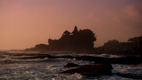 ocean waves crash against the rocks in the evening with tanah lot temple in the background, bali island, indonesia.