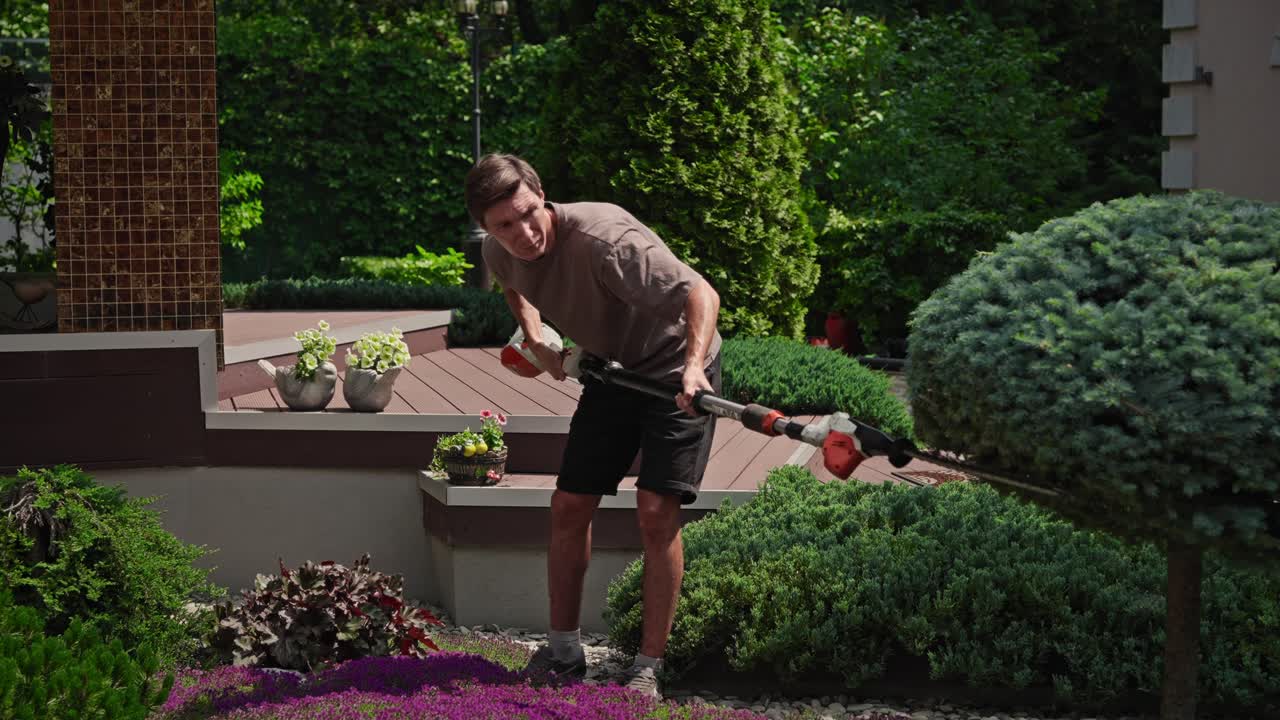 Man Trimming Bushes with a Long-Handled Hedge Trimmer in a Garden