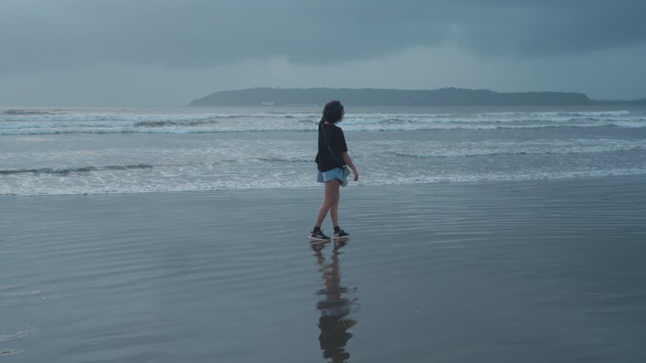 Person walking on a quiet beach under a cloudy sky, reflecting solitude