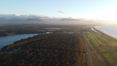 Drone-view-of-the-coast,-forests-Lake-Mahinapua-and-a-road-next-to-the-sea-during-sunset-at-Hokitika,-West-Coast,-New-Zealand