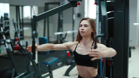 a pretty woman with flowing hair is sitting and doing exercise for the chest in the gym. professional equipment. healthy lifestyle
