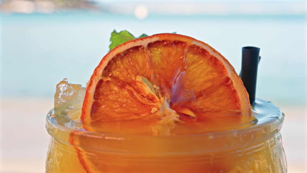 Primo piano di un cocktail arancione su un tavolo con una vista sfocata del mare sullo sfondo