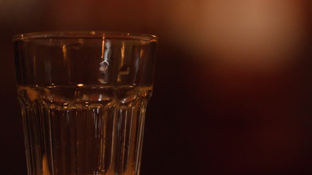 Acqua gassata trasparente versata in un bicchiere, con la creazione di bollicine su uno sfondo caldo e scuro da pub