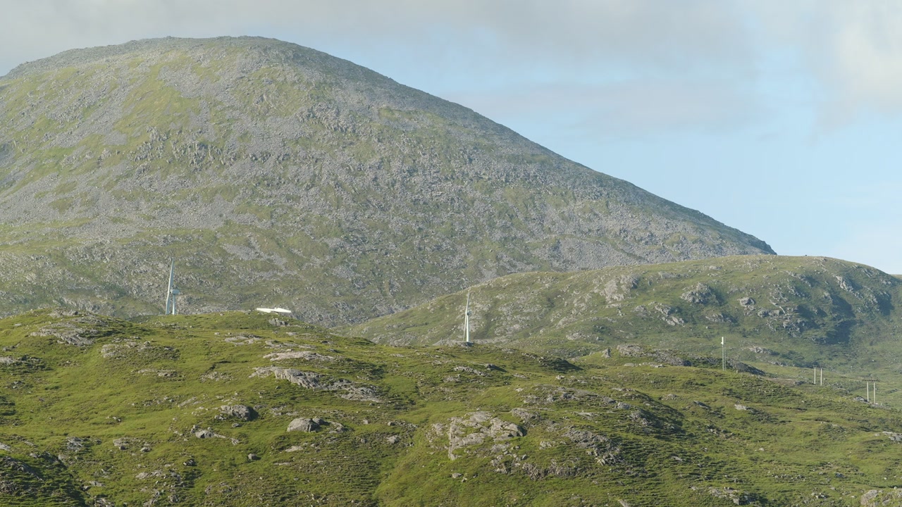 A shot of a mountain behind a wind farm on a hillside on the Isle of Harris.