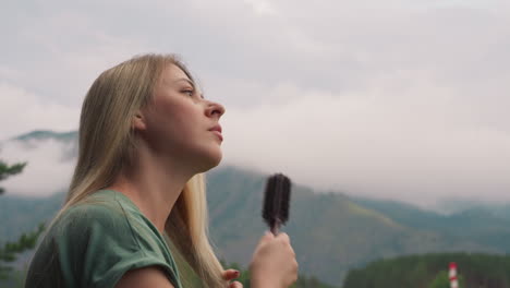 mujer pensativa cepilla el cabello de pie contra las montañas brumosas