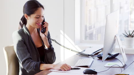 young asian woman on the phone smiling at her office desk