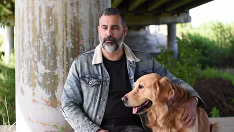 a serene moment of connection: a man and his loyal golden retriever enjoying a peaceful afternoon beneath an urban overpass surrounded by nature