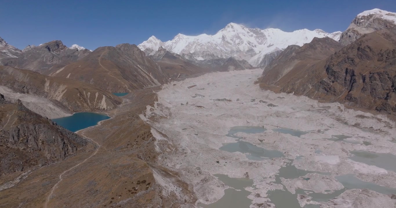 Glaciar Ngozumpa, Everest, Nepal, toma orbital panorámica con dron que revela pozas de agua de deshielo de color azul brillante en una morrena glacial rodeada de colinas inclinadas y el Cho Oyu cubierto de nieve al fondo