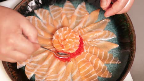 food plating - chef with teaspoon adding red caviars around the salmon rose on a round plate