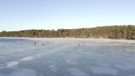 An-aerial-drone-shot-of-a-small-group-of-people-skating-on-a-large-solid-frozen-lake-during-the-daytime