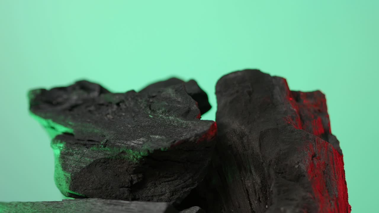 carbón de madera. madera natural o carbón negro tradicional en bucle en giratorio. fondo de pantalla azul o verde con luz led de color. disparo en estática. carbón para cocinar en la parrilla de la barbacoa. carbón negro.