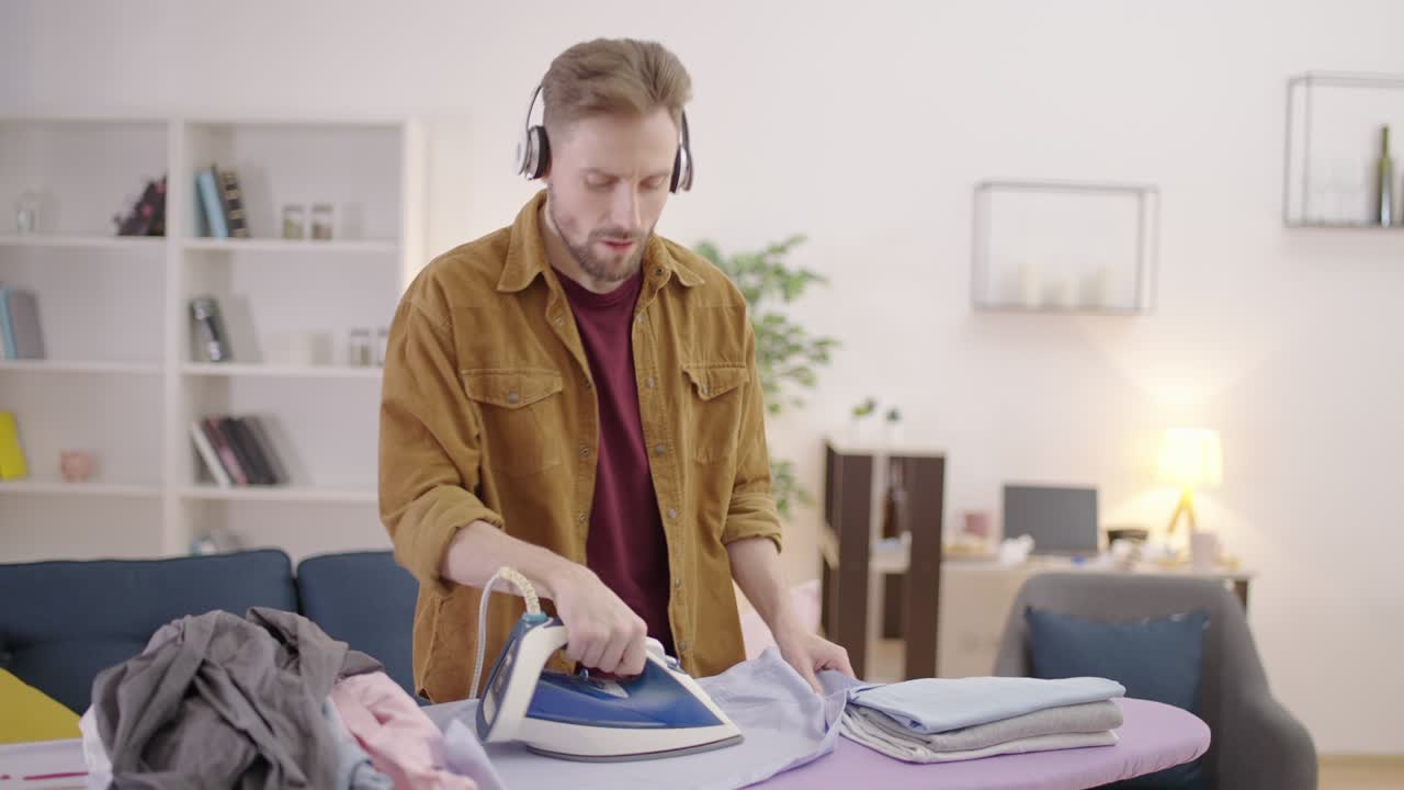 Marito con le cuffie che stira camicie, ascoltando musica e godendosi i lavori domestici