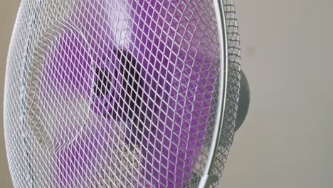 home appliance oscillating electric fan rotating purple plastic blades circulating air in room close up