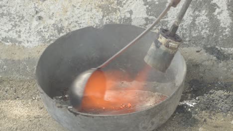 metal melting in a foundry ladle with a gas torch, industrial setting, close-up