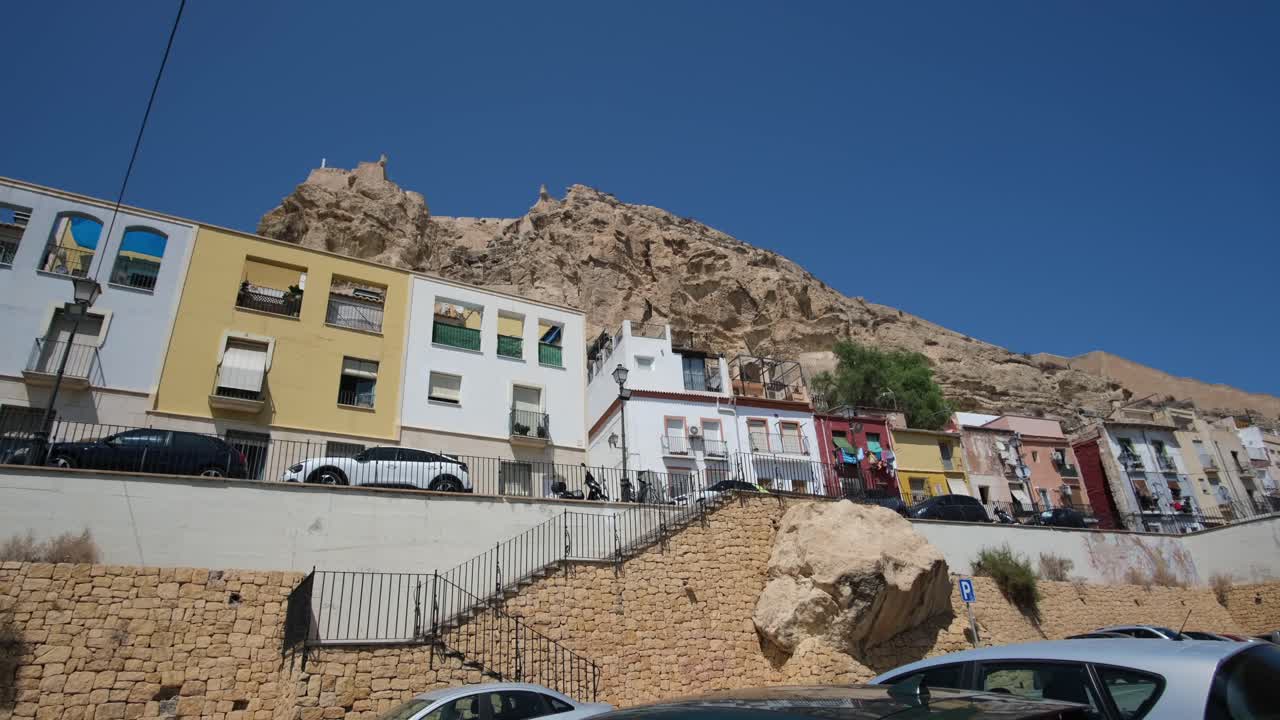 A stunning panoramic view showcases colorful homes nestled against the majestic backdrop of Castel De Santa Barbara in Alicante, blending vibrant city life with historic charm.