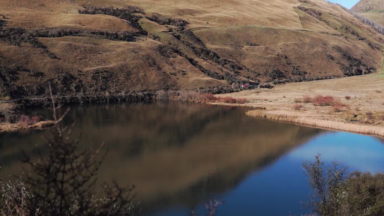 agua perfectamente tranquila en el lago rodeado de colinas y montañas onduladas de color naranja en el campo de nueva zelanda que causa reflejos nítidos