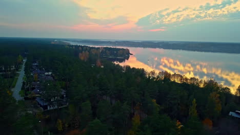 Cinematic-drone-shot-circling-around-and-revealing-the-majestic-autumn-landscape-of-Baltezers-estate-with-beautiful-sunset-sky-and-reflection-on-lake-river-tree-forest,-Latvia