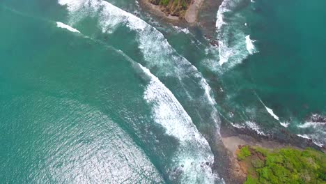 drone video tilting down over playa herradura where two islands nearly touch leaving a gap for the pacific ocean water to flow