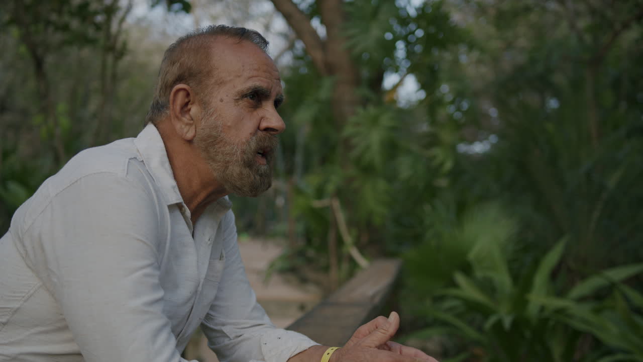 un hombre se apoya en una barandilla de madera, perdido en sus pensamientos mientras se pone el sol