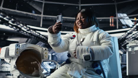 happy female cosmonaut doing videocall with family using smartphone in space
