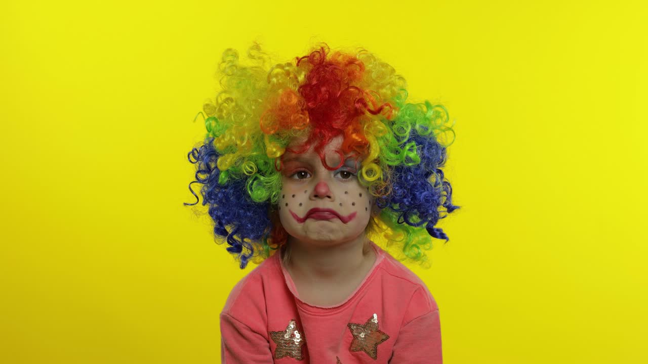 una pequeña niña payasa con una peluca colorida haciendo caras tontas, divirtiéndose, sonriendo, bailando. halloween