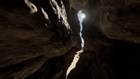 a narrow canyon with a bright sun shining through the opening at the top.