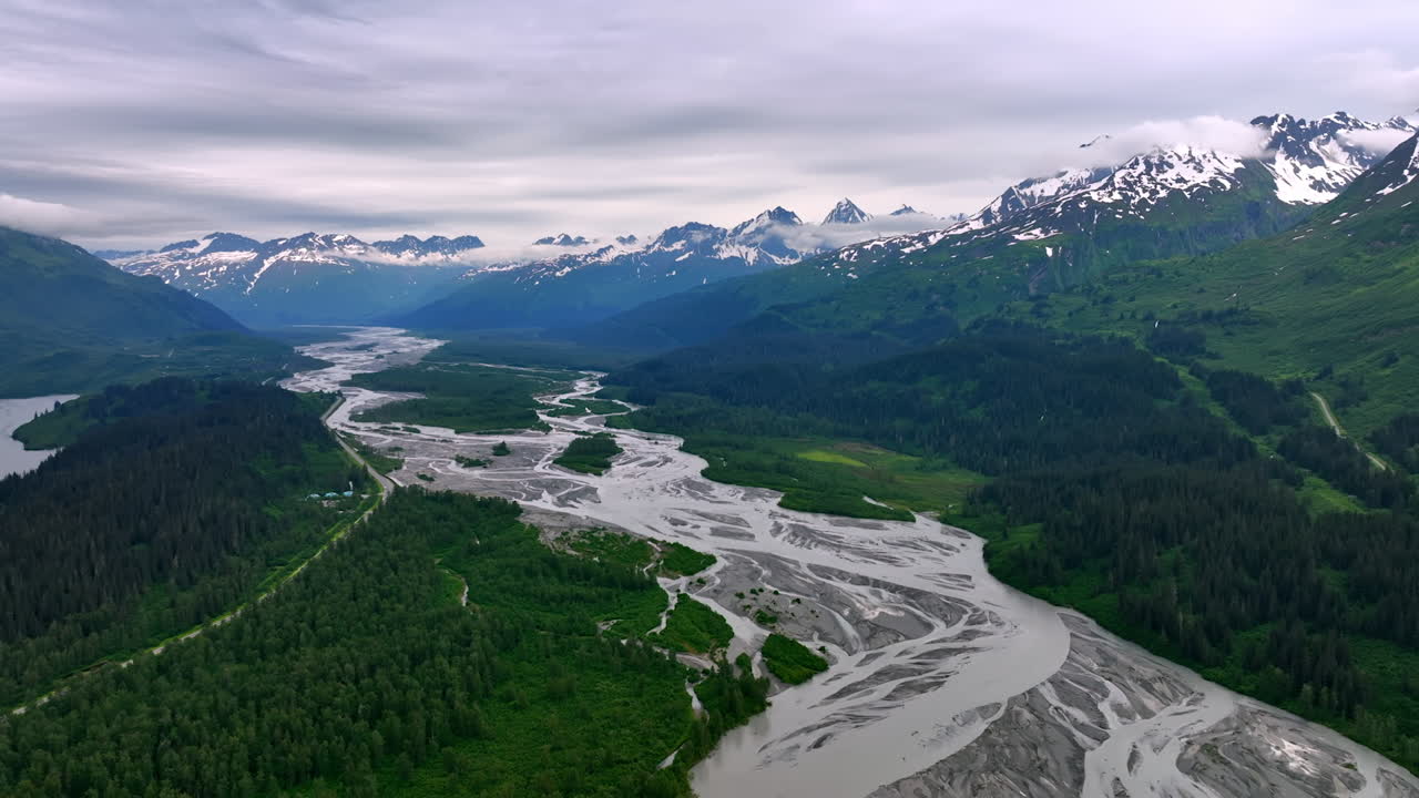 Braided river valley in Alaska mountains. Multiple silver channels of a braided river wind through forested valley toward peaks