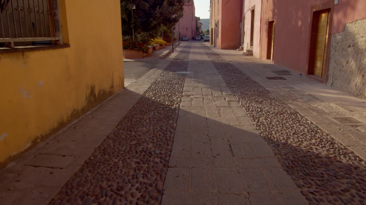 Rua de paralelepípedos e lajes de pedra cercada por edifícios históricos antigos na ilha da Sardenha, vista com movimento de câmera para frente e inclinação para cima.