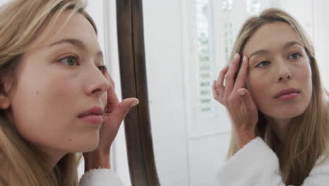 Biracial-woman-touching-her-face-looking-in-mirror-in-bathroom,-slow-motion