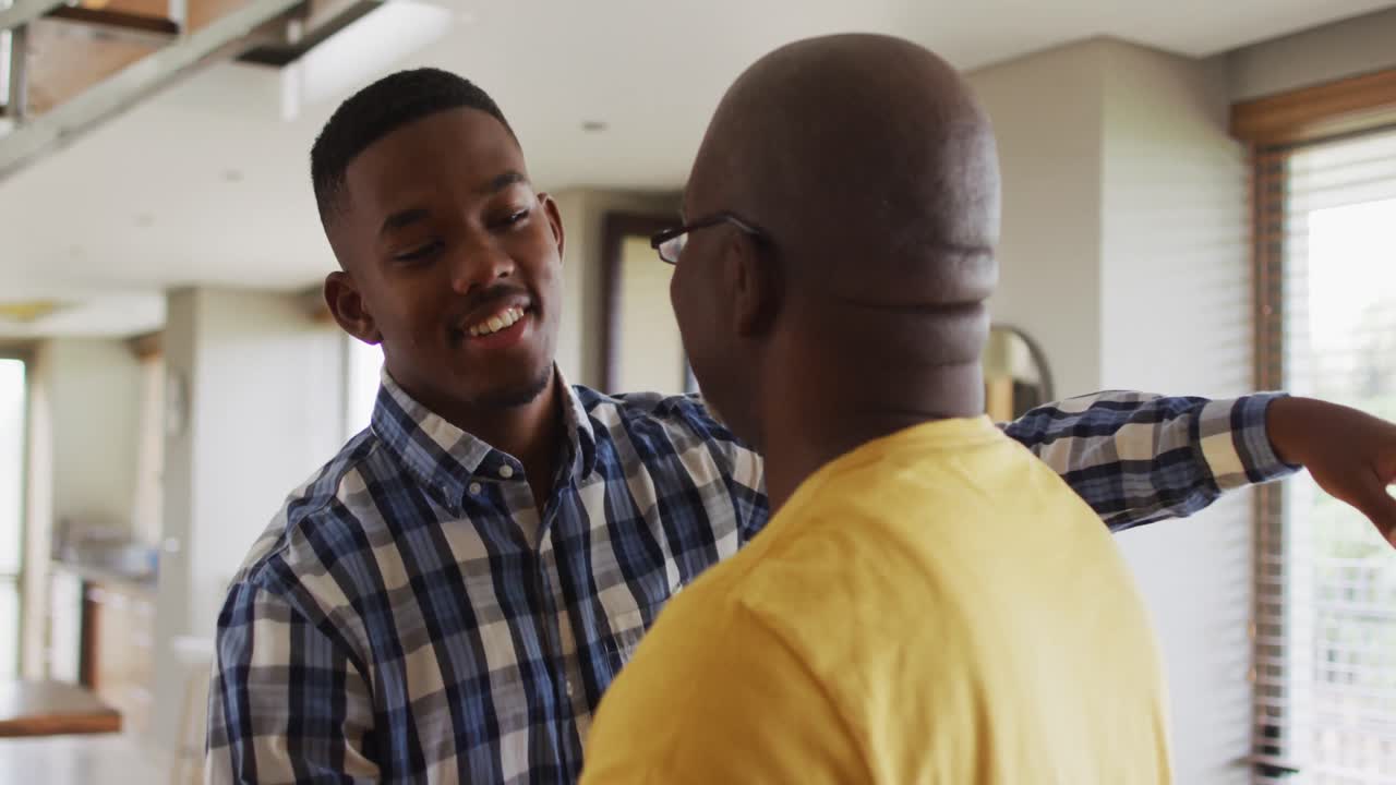 feliz padre mayor afroamericano abrazando a su hijo adolescente y sonriendo