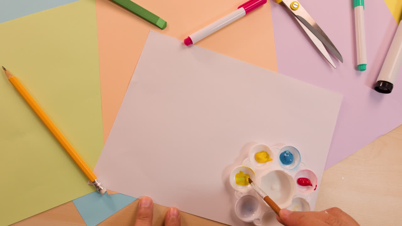 Artist hand dips brush in primary color palette on tidy desk with soft, even lighting