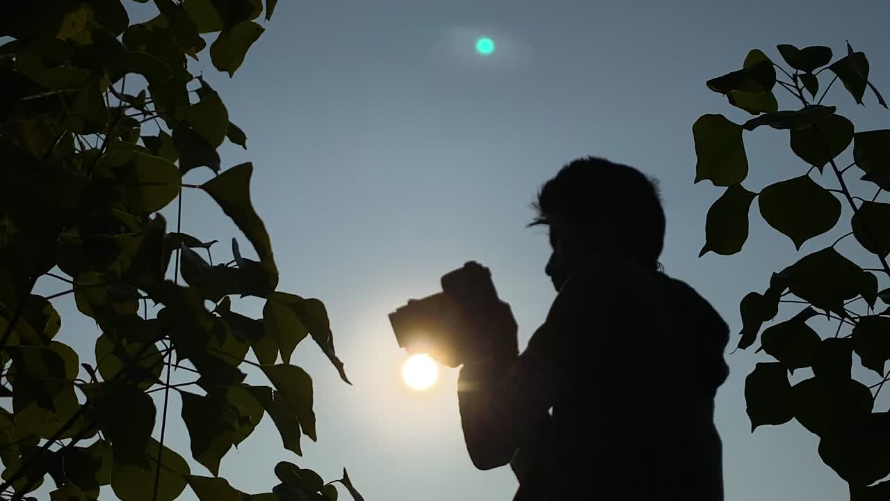 Closeup shot of young man taking photographs with DSLR camera, silhouetted