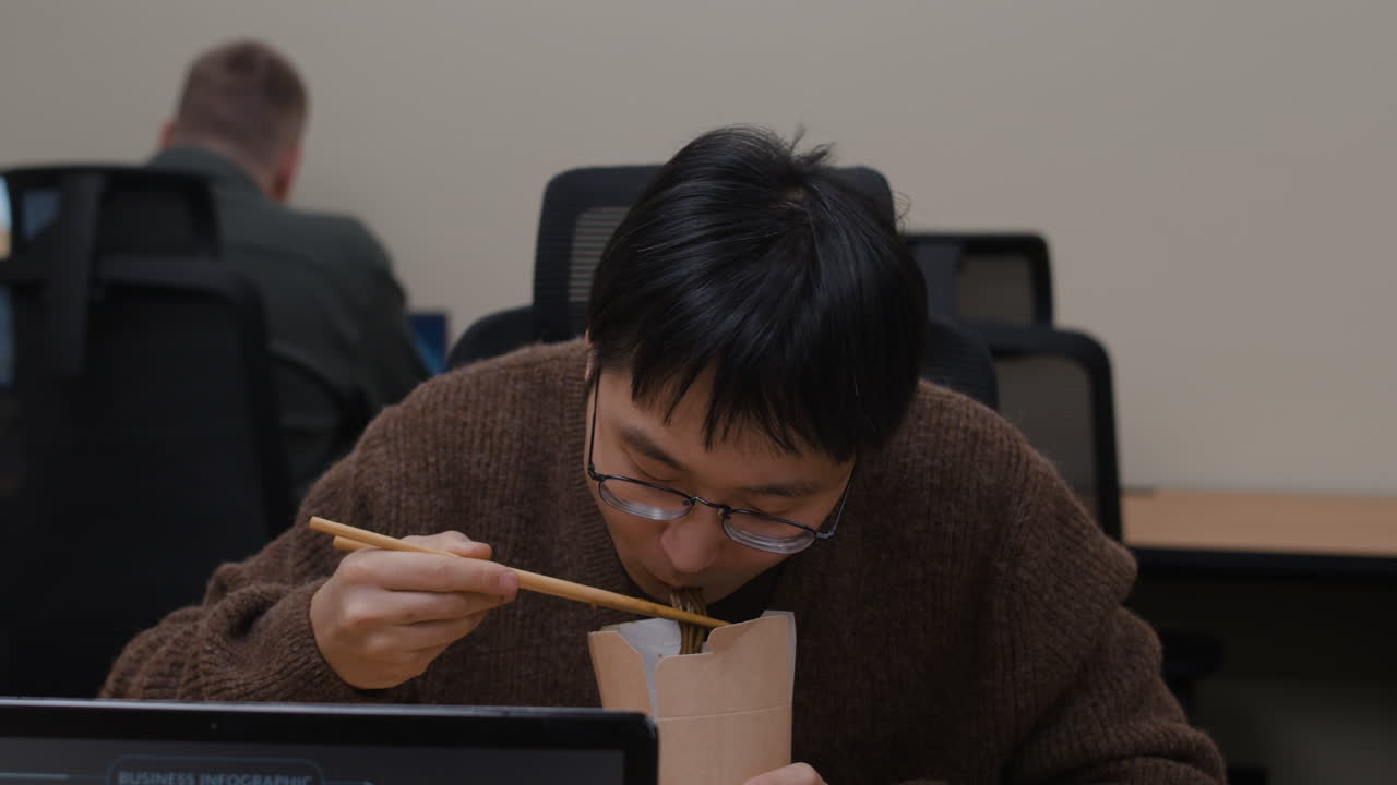 Man eating noodles at his desk
