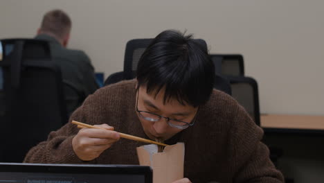 man eating noodles at his desk
