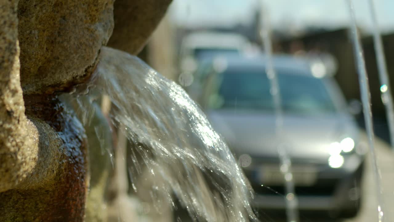 Água jorrando de uma fonte com um carro ao fundo
