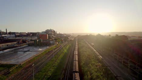 Railroad-train-passing-by-a-cotton-factory-at-sunset-in-Brazil---aerial-flyover