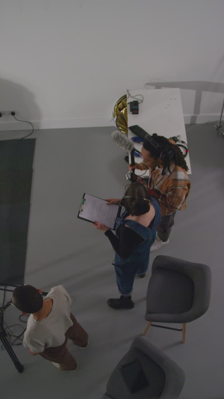 fotografía vertical de una directora con un asistente de producción y un grabador de sonido trabajando en un set de filmación filmando una película o un video en un estudio