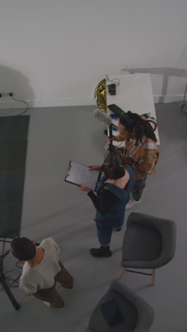 vertical video overhead shot of female director with production assistant and sound recordist working on film set shooting movie or video in studio