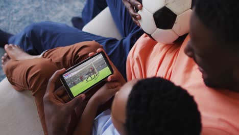 composite of father and son at home watching rugby match on smartphone