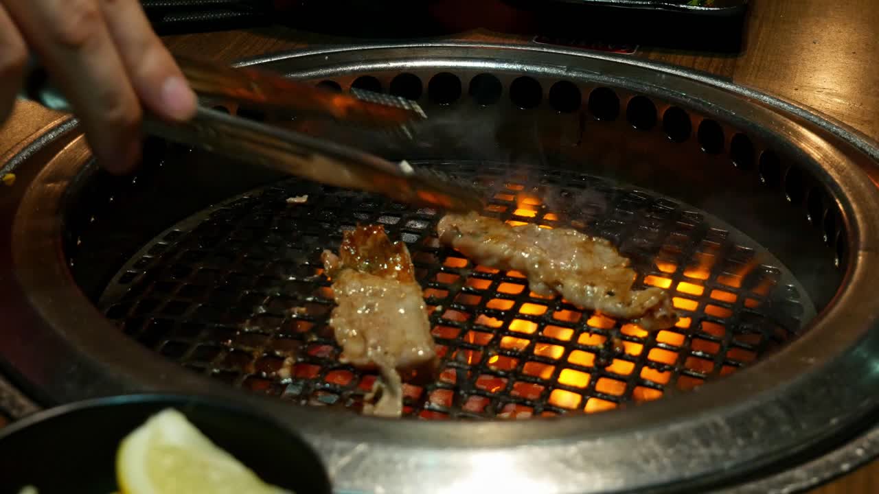 Turning over pieces of beed on yakiniku grill embedded into dining table at a Japanese BBQ restaraunt with tongues