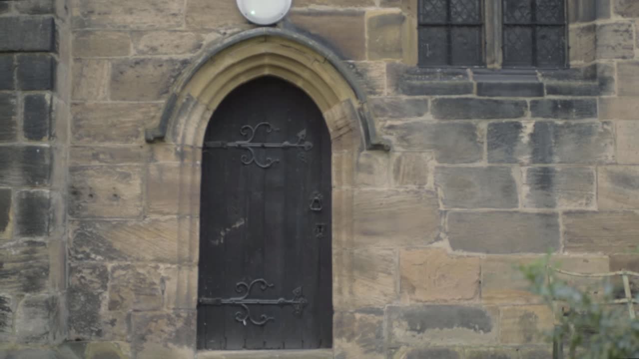 Gothic looking old black wooden door in stone church building wide panning