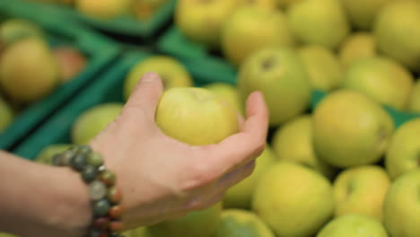 view of a close-up shot showing a hand wearing bead bracelets taking an apple from a crate in a grocery store. the action is captured with a handheld camera