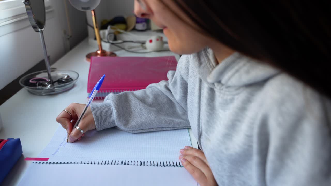 Girl writing down notes in a notebook, doing homework sitting at the desk