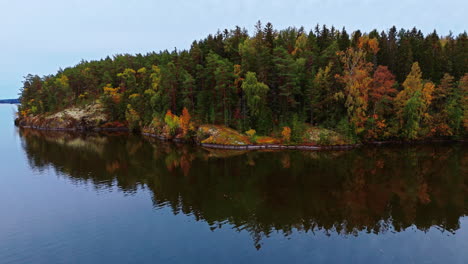 autumn forest on a lakeshore with green, brown, red and yellow trees reflected on the lake in valkeakoski, finland