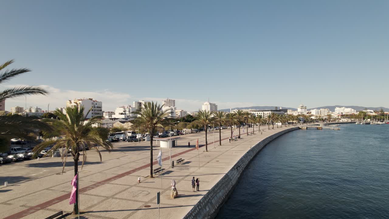 Ripresa aerea in allontanamento che rivela un lungomare panoramico sul fiume con palme, Portimão - Algarve.